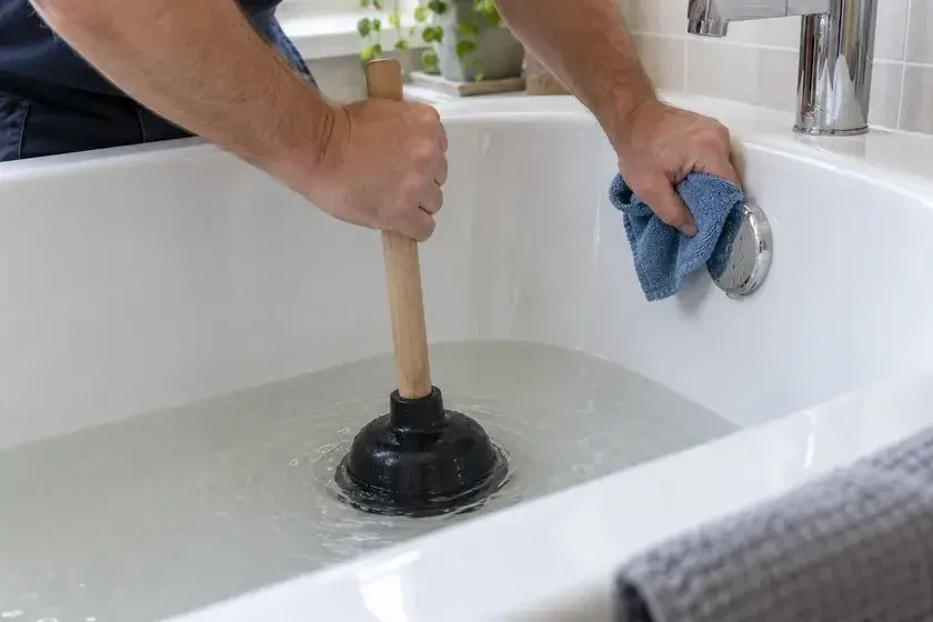 Hands using a plunger to clear standing water from a bath